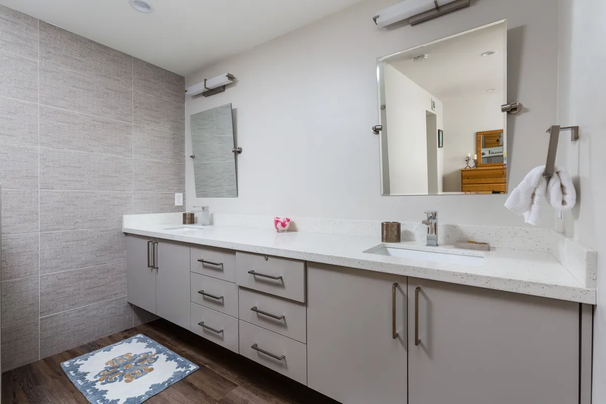 A contemporary en-suite bathroom with a double vanity, expansive mirrors, and a textured accent wall. The room is organized and calming, with a decorative rug adding warmth to the sleek design.