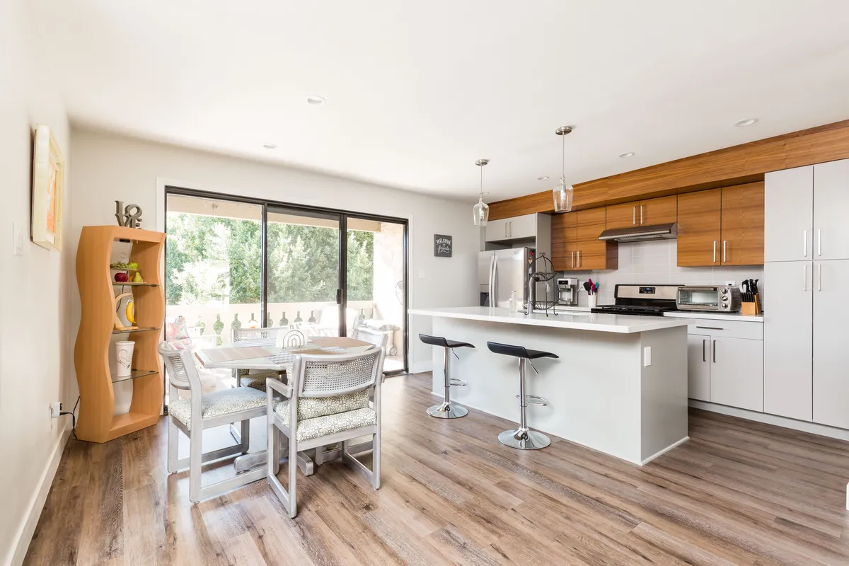 A bright and cheerful open-concept kitchen and dining area featuring a central kitchen island, a dining table set for a meal, and large windows filling the space with natural light. The scene is welcoming, with details suggesting both everyday and special gatherings.