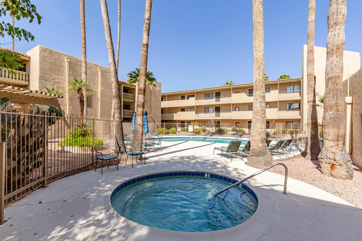 This exterior image captures a vibrant swimming pool area surrounded by palm trees and accented with a relaxing hot tub. Lounge chairs are placed around the pool, creating an inviting space for both swimming and sunbathing. The scene is bathed in warm sunset light, evoking a sense of relaxation and enjoyment.